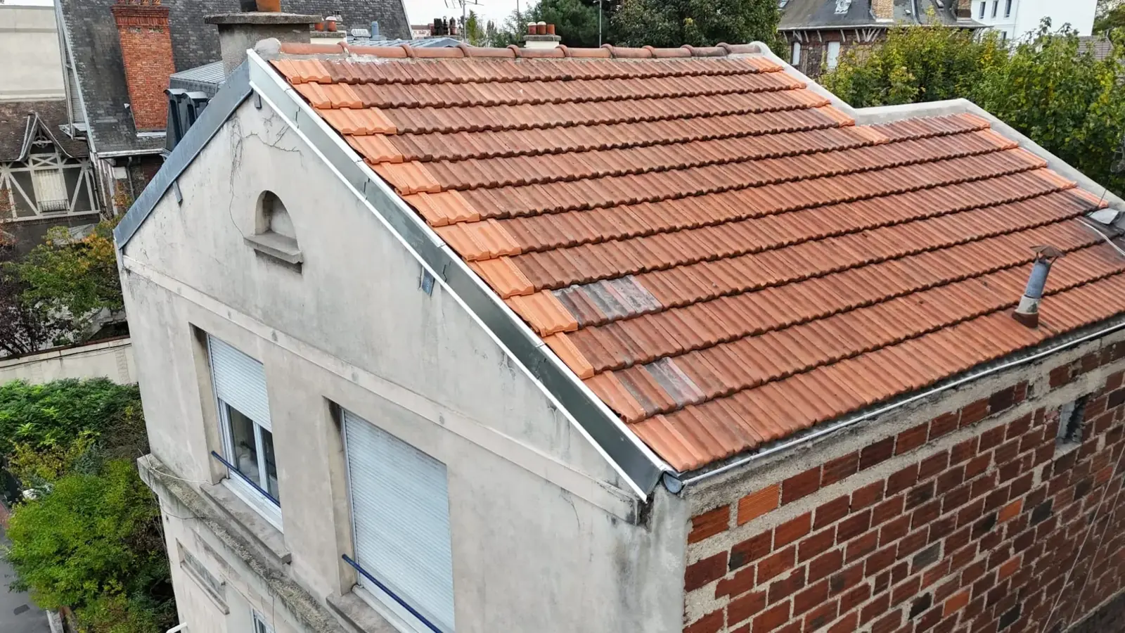 Toiture en tuiles rouges vue d’en haut, au-dessus d’une façade claire